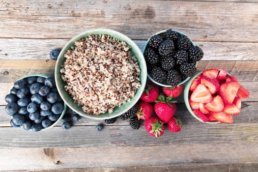 Flat lay of fres strawberries, blueberries, blackberreis and quinoain bowls.