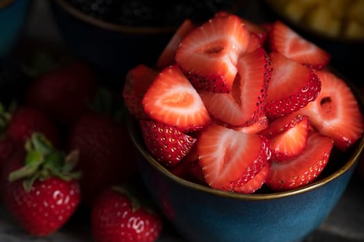 Close up of fresh sliced strawberries in blue bowl low key.
