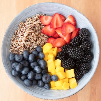 Blue bowl with quinoa,  strawberry slices, chopped nectarines. blackberries and blueberries on wooden surface, image 6 of 8