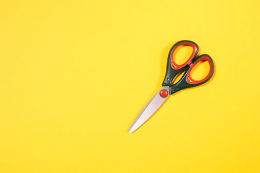closed black scissors with red elements on yellow background