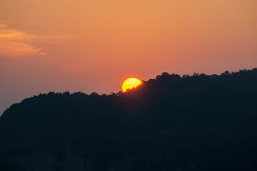 Sunrise behind the mountains, the shadows of the mountains, the orange sky with faint clouds.