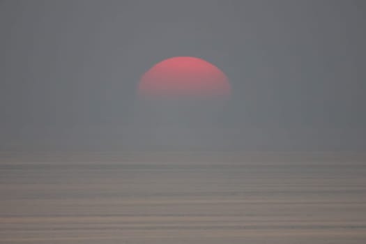 The sun is falling into the sea and being partially swallowed by the fog.  sky  is dark