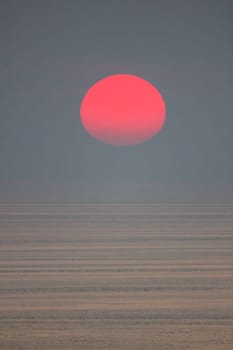 The sun is falling into the sea and being partially swallowed by the fog.  sky  is dark