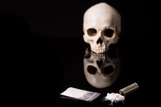 cocaine, Herion or other illegal drugs that are sniffed by means of a tube or injected with a syringe, money and Skull, isolated on black glossy background