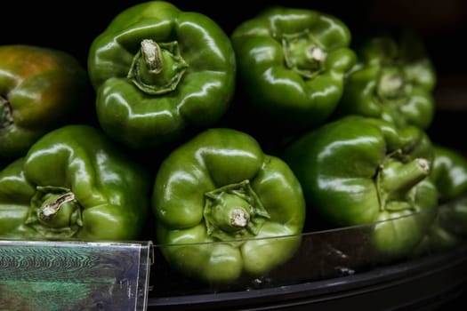 A close-up shot of an abundance of fresh green peppers on display at a market stall.