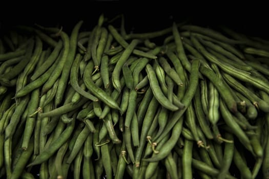 A close-up shot of an abundance of fresh green pea pods on display at a market stall.