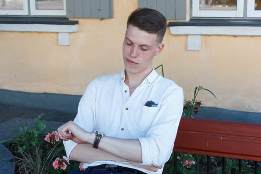 Young man relaxing on park bench and looking at his watch