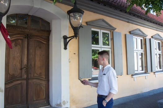 Young man with mobile phone in hand standing at the big wooden door