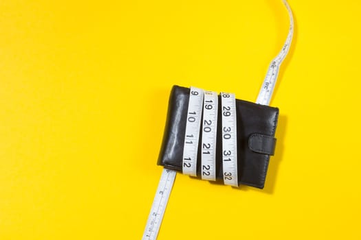concept of budget and money. Purse is tied with measuring tape on yellow background