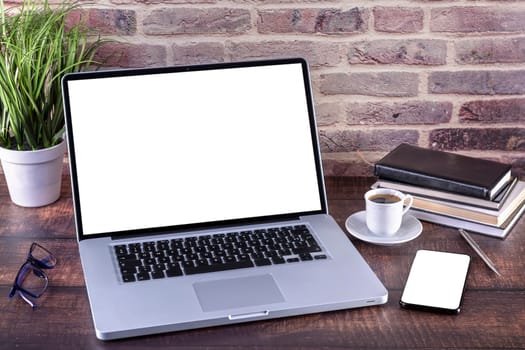 Laptop notebook with blank screen and cup of coffee and notepad pen and books and smart-phone on wooden table. Mock up on wooden table with laptop with blank screen, cup of coffee, pen, books and flower. Focus on keyboard.