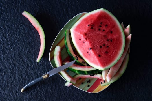 Piece of watermelon with cut slices and eaten on a plate with a knife on a black background