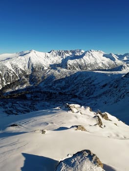 View from the top of Todorka Peak to the Pirin mountains ridge covered by snow in a sunny winter day with blue sky.