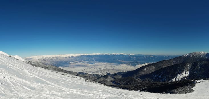 Panoramic view from the top of Pirin mountains to the Bansko city in Bulgaria. Cold winter day, snowy peaks and clear blue sky.