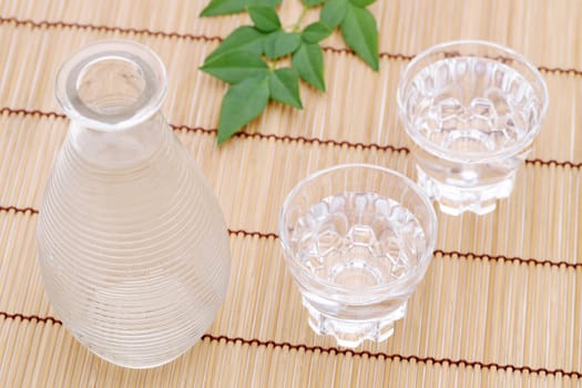 Japanese sake in transparent glass cup and jar on bamboo table