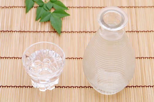 Japanese sake in transparent glass cup and jar on bamboo table