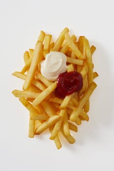 portion of golden fried potato chips, pommes frites or French fries with mayonnaise and ketchup dressings viewed top down isolated on white