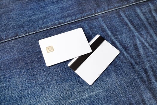Two bank plastic bank cards on denim background. White credit cards. Front and back view.