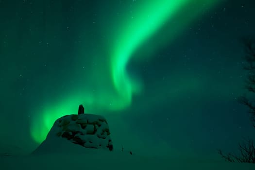Awesome display of aurora borealis northern lights above the stone marker on the border between Finland and Norway