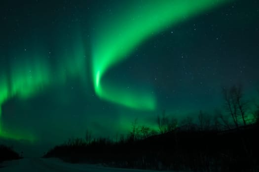 Awesome display of aurora borealis northern lights above empty snow covered road in Norway and Finland
