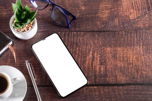Working table with smartphone notepad coffee cup pen glasses plant on wooden table