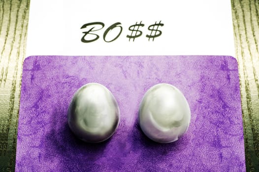Two metal eggs on the office desk opposite the word Boss. The concept of power
