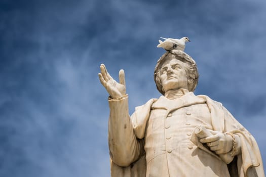 White bird sitting on top of ancient statue of Dionysios Solomos in Zakythos Town square, Greece