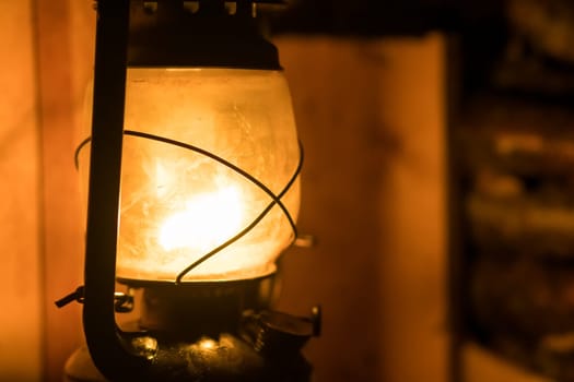 Old lit kerosene lamp hanging from a wooden beam in a shed in a village, northern Norway