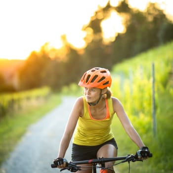 Pretty, young woman biking on a mountain bike enjoying healthy active lifestyle outdoors in summer (shallow DOF)