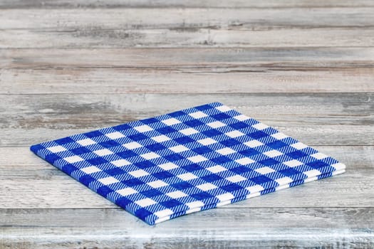Empty table background. Closeup of a empty blue and white checkered kitchen cloth, textile, tablecloth or napkin on a rustic bright gray table. Template for food and product display montage. Macro.