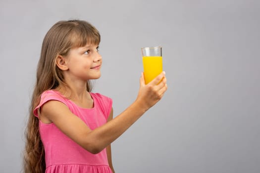 A girl holds a glass of juice in her hand and looks at the empty space on the right