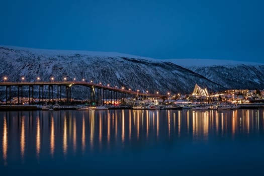 Tromso, Norway -  December 2018 : Port and harbour with famous Tromso Bridge across Tromsoysundet strait in the background, photographed at night