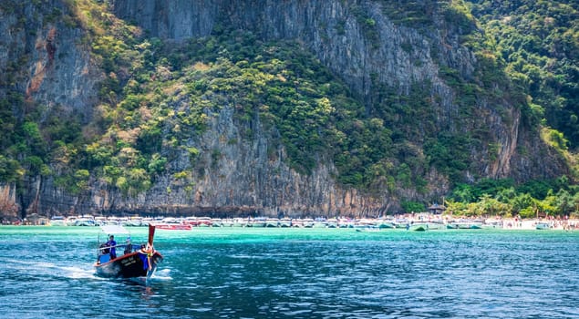 Phi Phi Lay island, Thailand, March 2013 Long tail boat departing from crowded beach of Maya Bay, one of the iconic beaches of Phi Phi islands