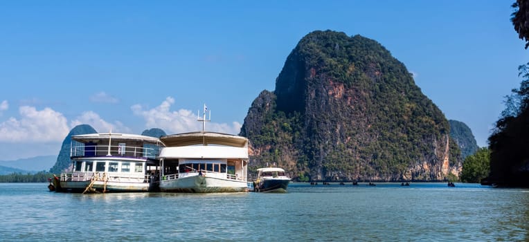 Large cruise boats docked on anchor near islands with high mountains in Phang Nga peninsula, people canoeing around islands, Thailand