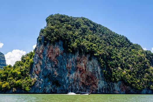 Single long tail Thai boat next to Phi Phi island, green trees and high cliffs in background, Thailand, view from see