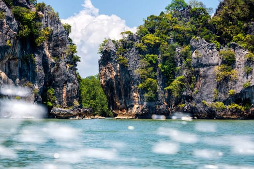 View on large cliffs and mountains of islands in Phang Nga archipelago, motion blurred splash of water from speed boat, Thailand