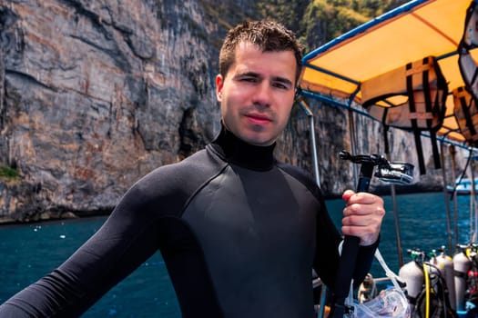 Young Caucasian male scuba diver holding action camera and preparing for diving from boat full of scuba gear, Phi Phi Island, Thailand
