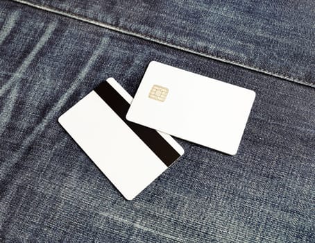 Photo of two blank credit cards on gray denim background. White bank cards. Mockup for branding identity. Copy space for placing your design.