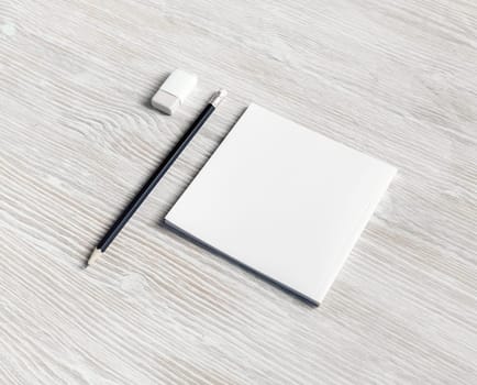 Photo of white square booklet, pencil and eraser on light wood table background.