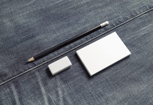 Photo of blank white name card, pencil and eraser on denim background. Copy space for text.