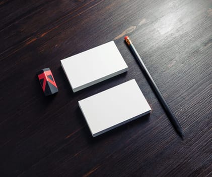 Blank office stationery. White business cards, pencil and black eraser on dark wooden background.