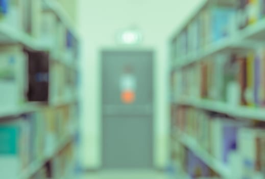 Blurred abstract background of bookshelves and interior of college or university library with textbooks and emergency exit. Vintage color image.
