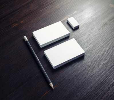 Blank stationery set. White name cards, pencils and eraser on dark wooden background.