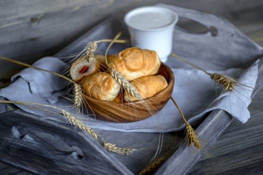 Croissants, a cup with kefir and ears of grain on a wooden tray. The concept of a wholesome breakfast