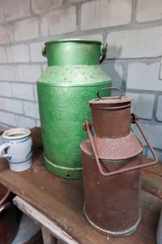 An old green tin can beside a rusted tin can on a shelf in front of white bricks wall.