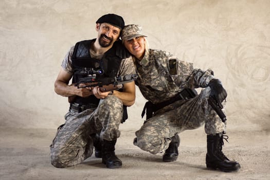 The smiling male and female military persons in military uniforms are looking at camera on gray wall background.