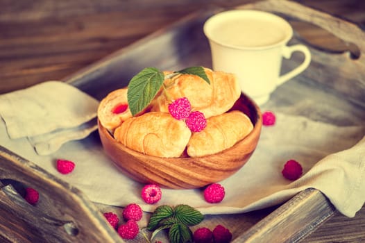 Croissants with raspberries on a wooden tray. The concept of a wholesome breakfast