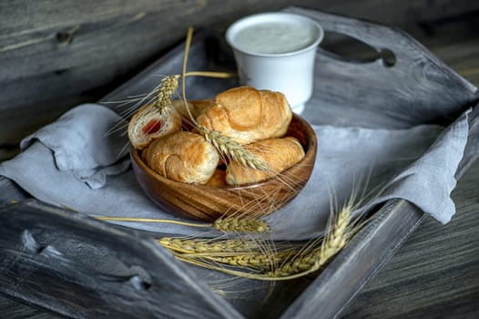 Croissants, a cup with kefir and ears of grain on a wooden tray. The concept of a wholesome breakfast