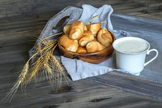 Croissants, a cup with kefir and ears of grain on a wooden tray. The concept of a wholesome breakfast