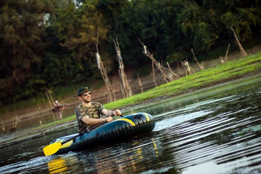 The oarsman is rowing in inflatable boat on shallow lake in nature.