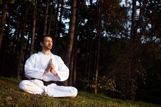 Man in white kimono is practicing meditation in nature in forest.